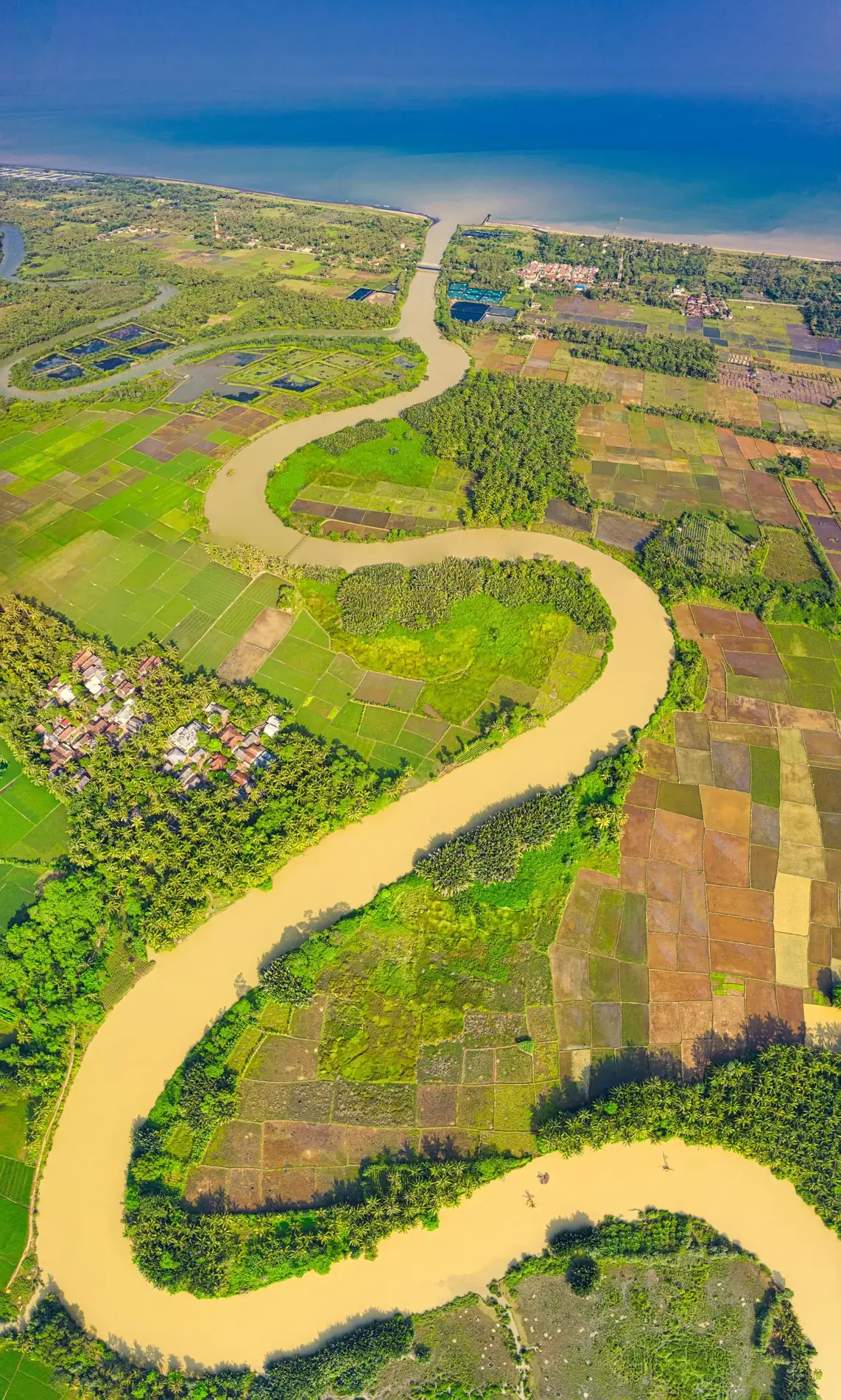 An aerial river crosses farmland on its way toward the coast